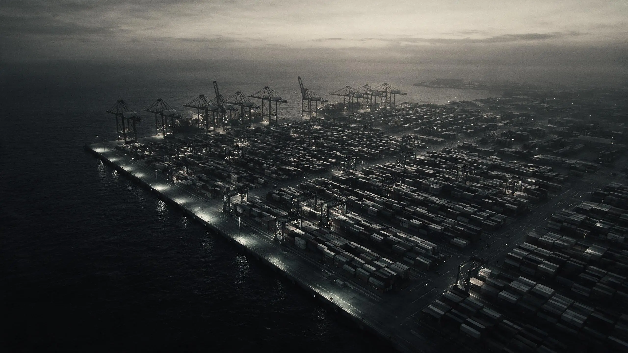 Aerial view of a container terminal at dusk, with cranes along the quay and containers laid out in rows.