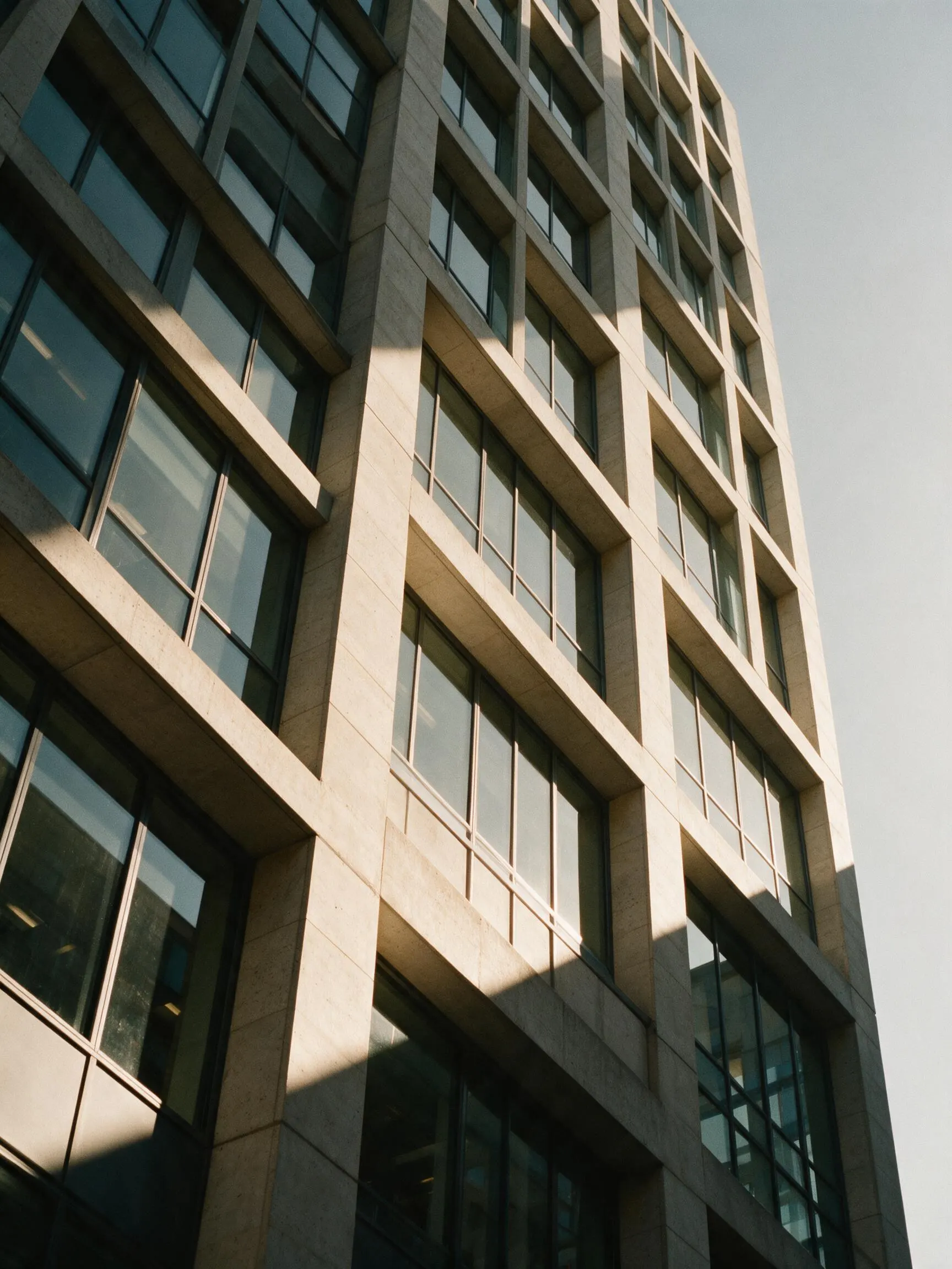 Sunlight raking across the stone and glass facade of a modern office tower.